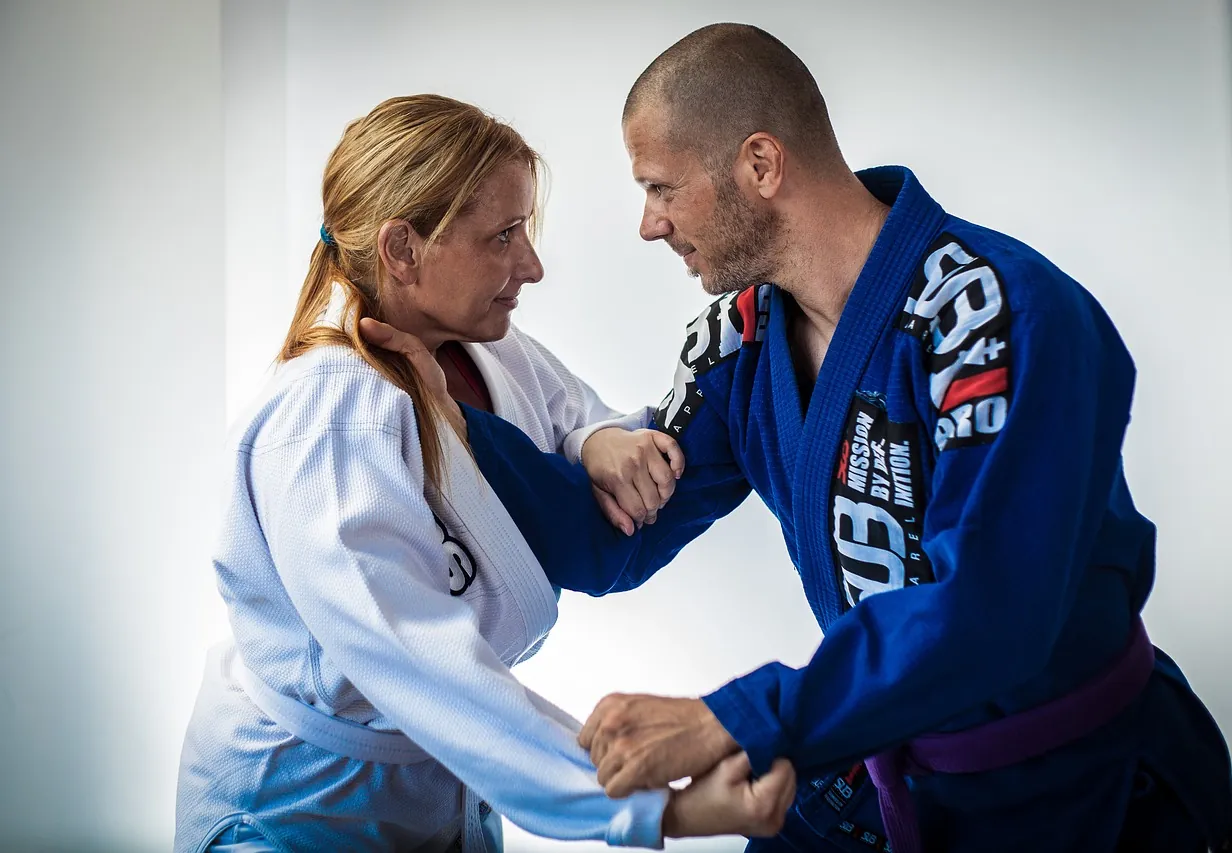 Een man en een vrouw in een judopak oefenen een greep tijdens een jiu-jitsutraining.