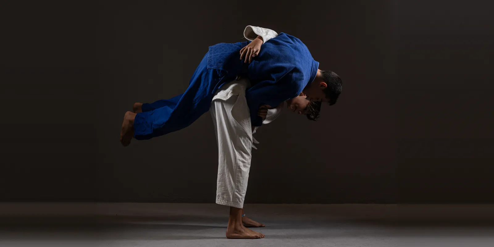 Een judoworp: een judoka in een wit pak tilt zijn tegenstander in een blauw pak over de heup.